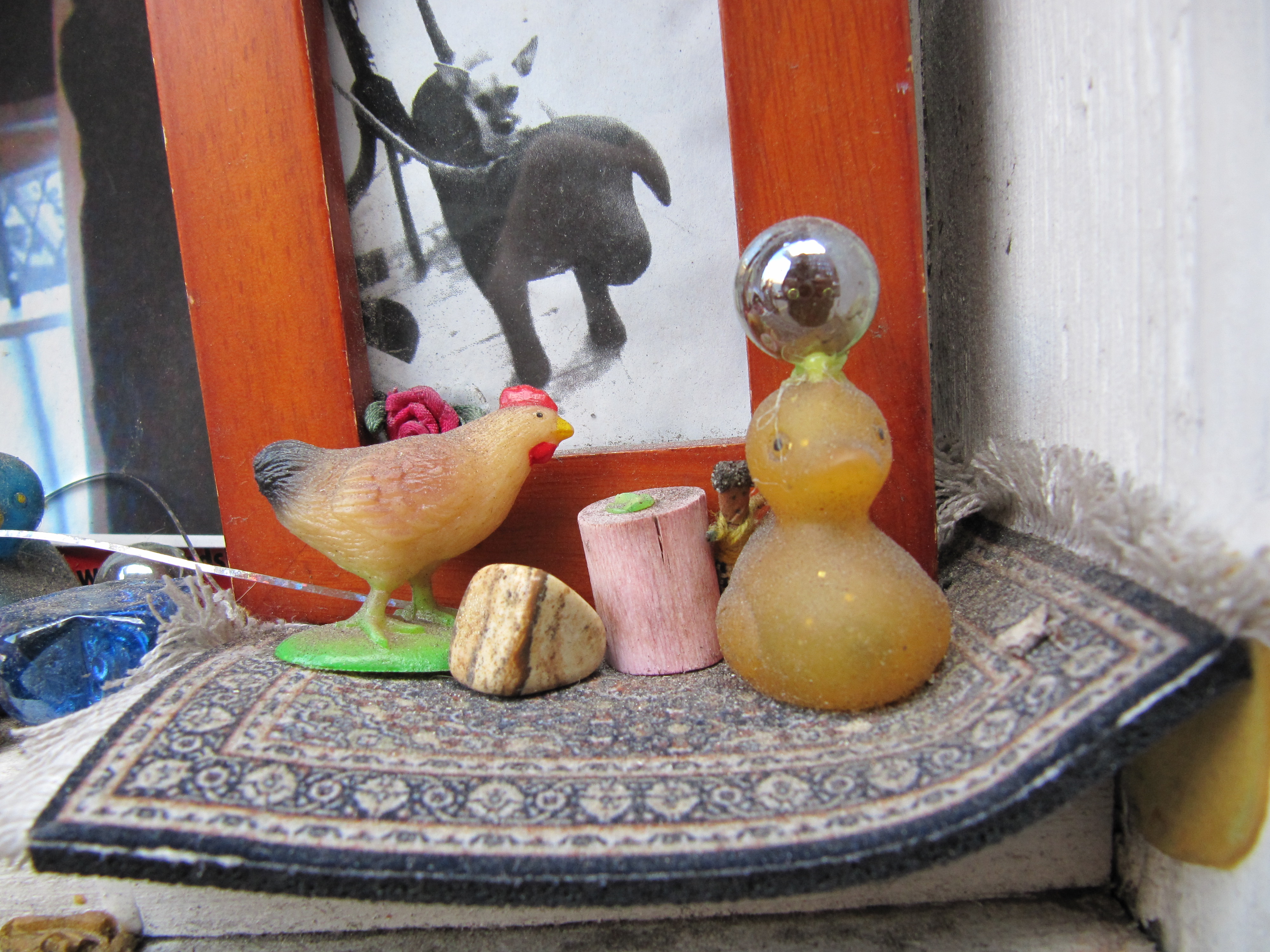 A closeup on tiny rubber duck, rooster, and stone on a tiny carpet