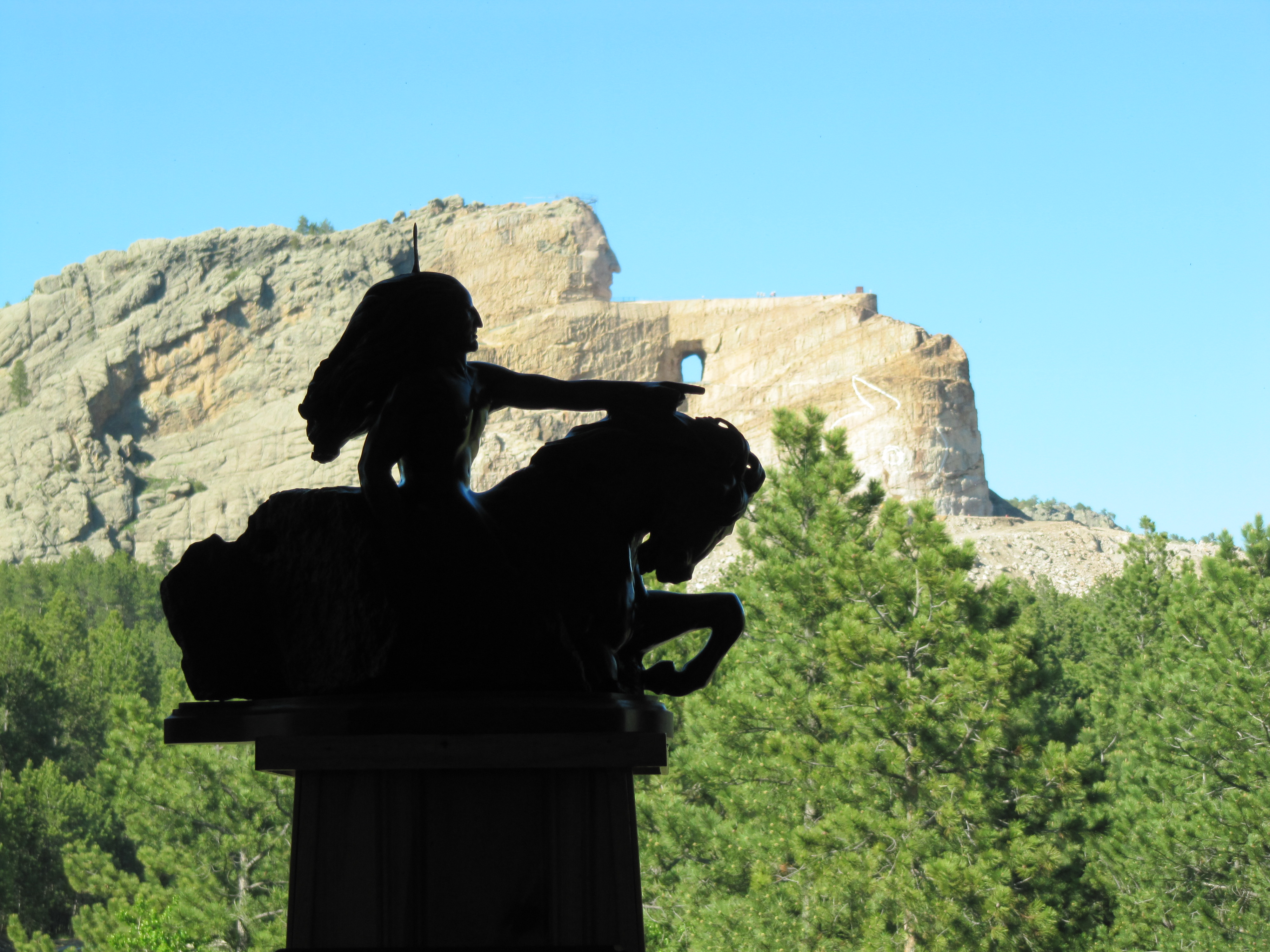 A silhouette of the projected crazy horse sits in front of the actual sculpture